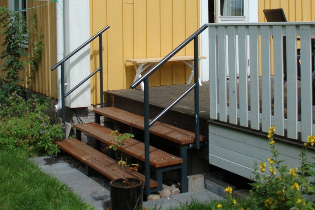 Eine Stahltreppe mit Holztrittstufen führt hinauf zu einer Veranda.