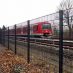 Sicherheitszäune an Bahnstrecken: Stahlmattenzaun an der Bundesbahnstrecke in Halstenbek mit roter S-Bahn im Hintergrund.
