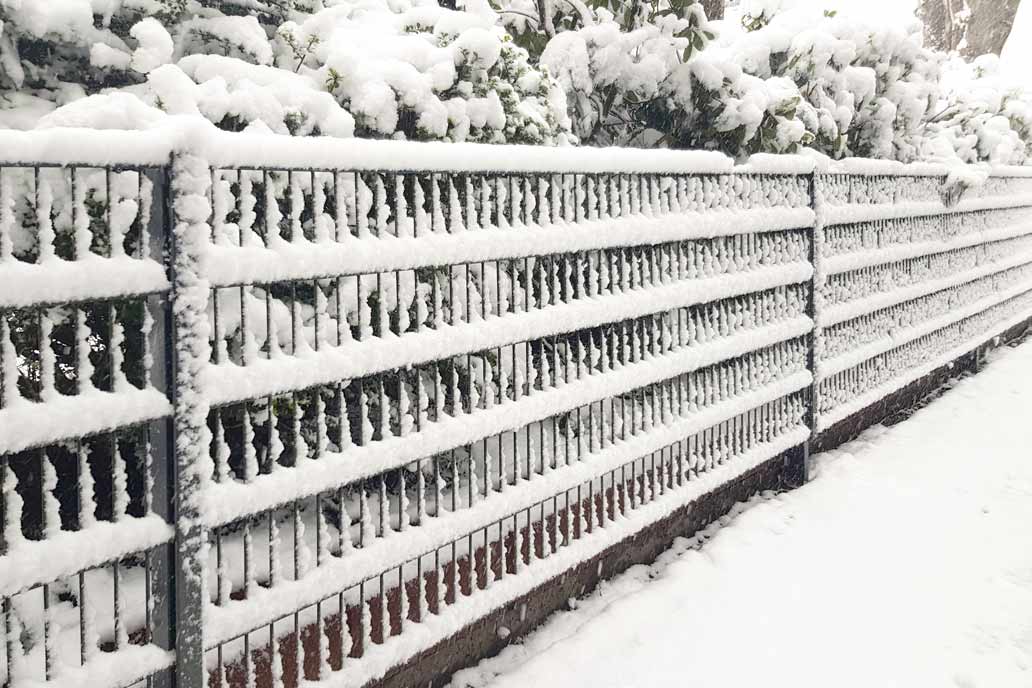 Schnee auf allen Stäben eines Stahlmattenzauns.