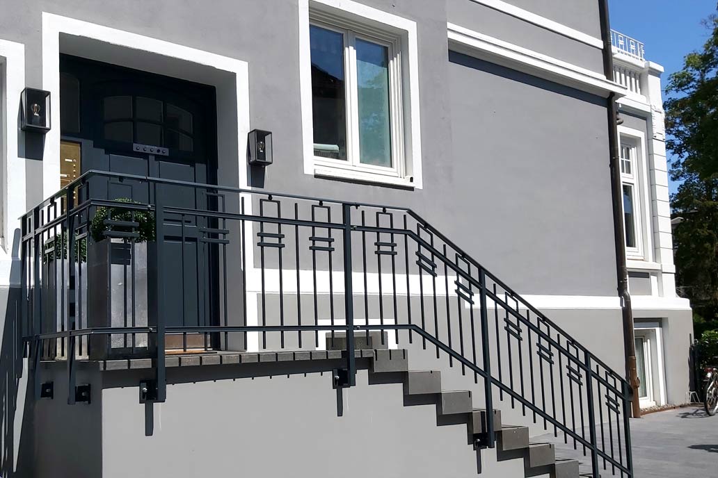 Neues Treppengeländer aus Stahl an einer Treppe zu einem grau gestrichenen Gründerzeithaus.