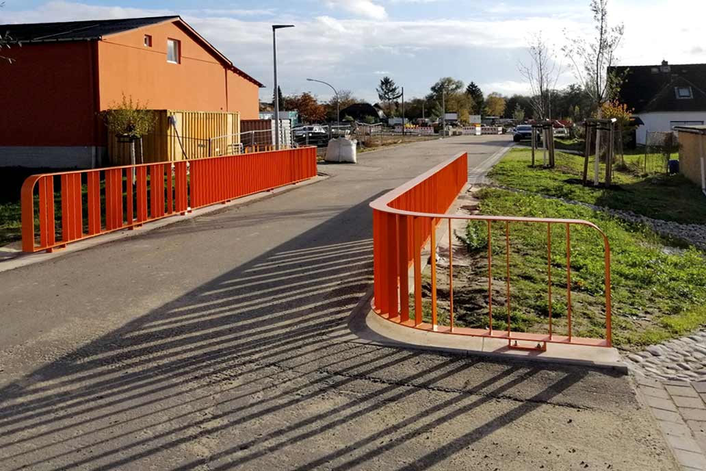 Ein orangenes Geländer Georgswerder Kirchwiese sichert die Straßenquerung über das Mulden Entwässerungssystem.