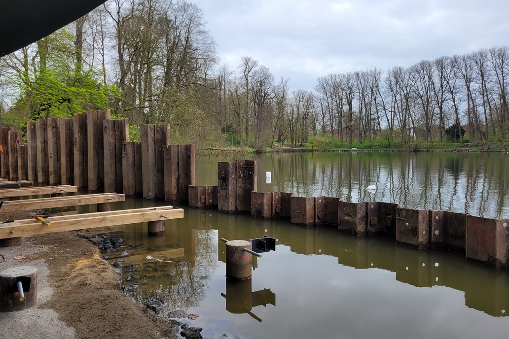 Blick auf die Baustelle der neuen Tribüne am Eutiner See. Am Ufer, teilweise im Wasser, Bohrpfähle mit angeschweißten Stahlkonsolen. An einigen ist schon der Holzunterbau für den Steg befestigt.