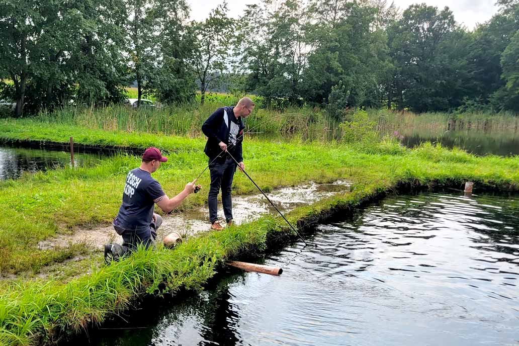 Ein Kollege von Gawron angelt, der andere hebt den gefangenen Fisch mit dem Kescher aus dem Wasser.