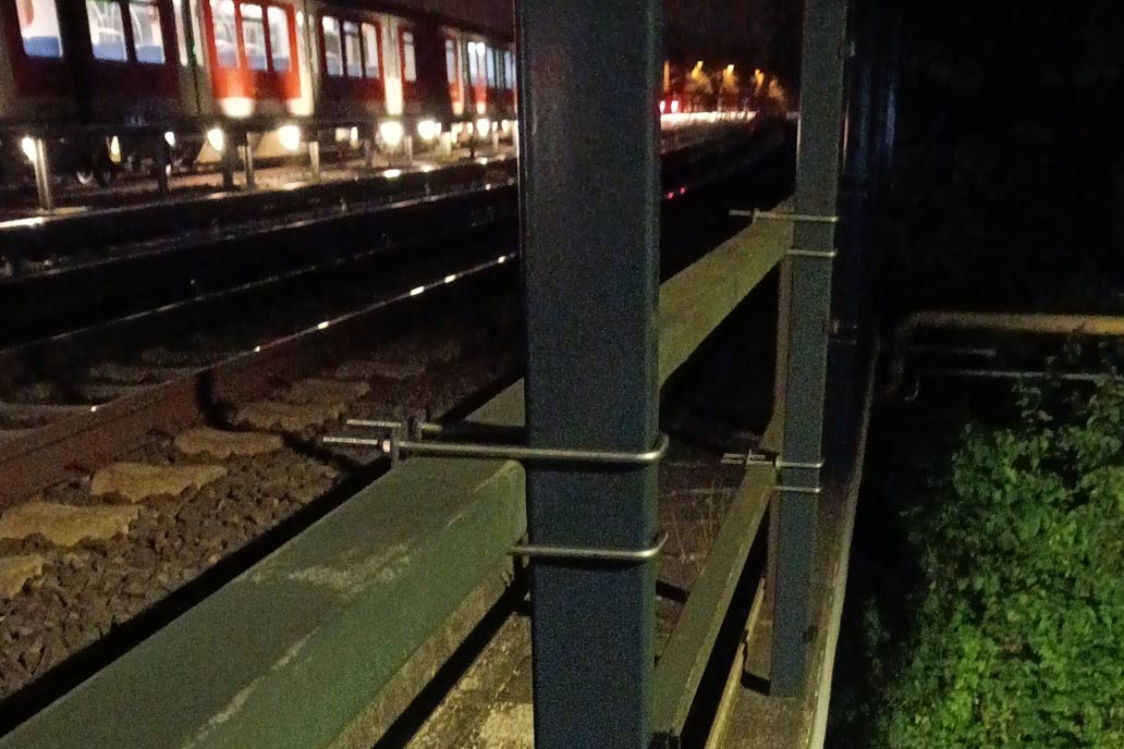 Neue Zaunpfosten an einer Gleisanlage der S-Bahn in Hamburg werden mit Bügeln an einem bestehenden Geländer befestigt.