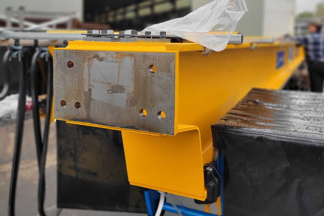 Ein orange-gelb beschichteter Hauptträger mit der unbeschichteten Stelle, an die der Fahrwerksträger der Brückenkrane geschraubt  wird.