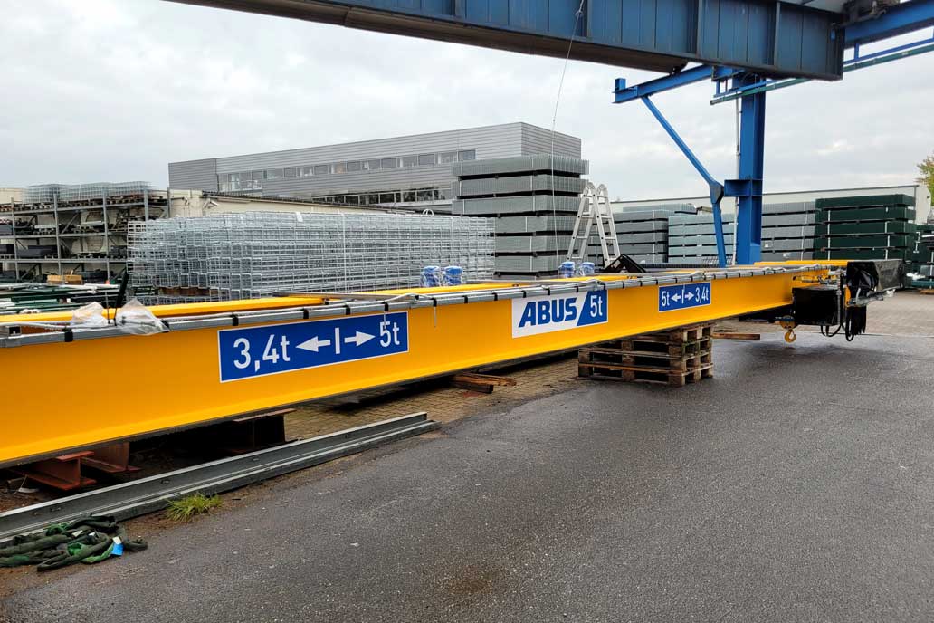 Die orangene Stahl Brücke für einen der beiden Brückenkrane liegt auf dem Hof vor Stapeln mit Zaunmatten und wird gleich eingebaut.