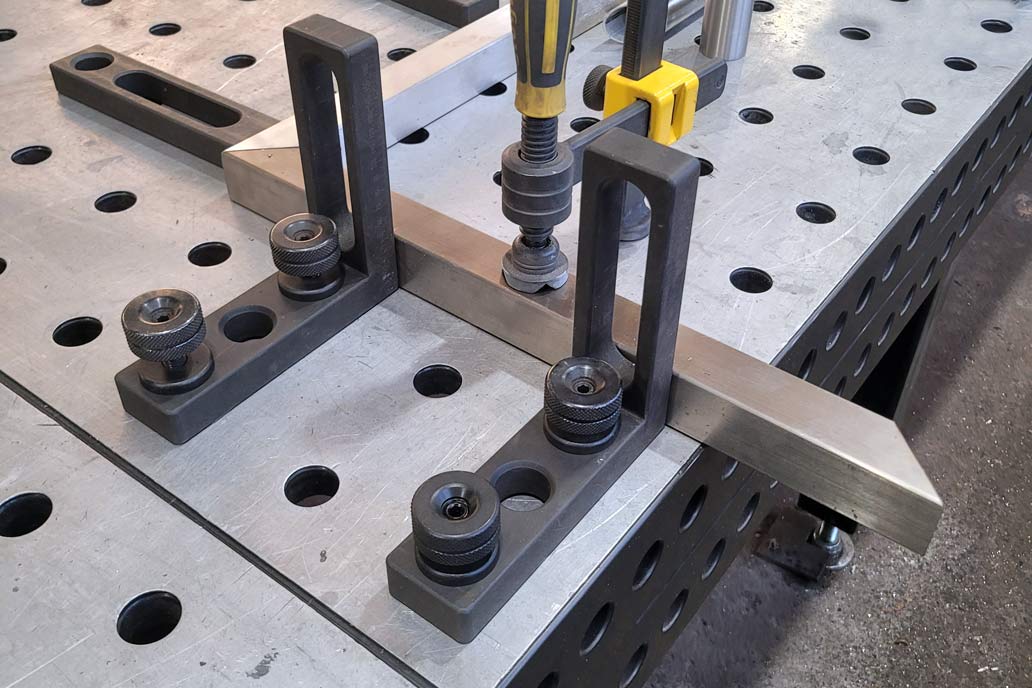 Ein dunkelgrauer Schweißtisch mit Löchern, in denen Bolzen und Zwingen das Werkstück präzise an seinem Platz halten. zur Befestigung von Metallbauteilen in der Edelstahl-Werkstatt von Gawron.