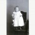 Ein etwa ein Jahr altes Kind in einem weißen Kleid steht auf einem Stuhl. Das Foto sollte von 1905 sein und ist schwarz-weiß.