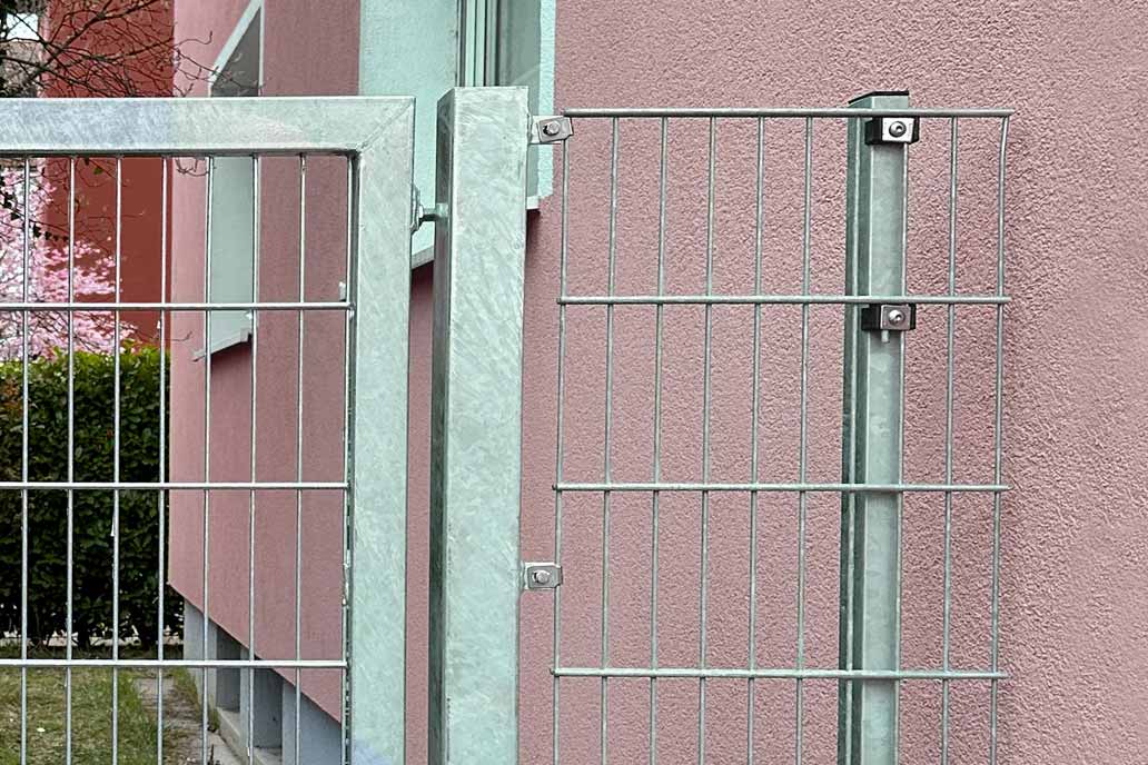Eine Zauntür mit Wandanschluss an die altrosa verputzte Fassade eines Mehrfamilienhauses.