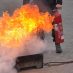 Brandschutzschulung auf dem Hof des Metallbauerunternehmens Gawron: Eine orange lodernde Flamme, dahinter ein Mann mit einem Feuerlöscher.