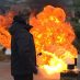 Eine orange-gelbe Wolke bei einer Fettbrandexplosion im Rahmen der Brandschutzschulung beim Metallbauunternehmen Gawron. Im Vordergrund steht ein dunkel gekleideter Mann, der kurz zuvor an einer langen Stange etwas Wasser in brennendes Öl geschüttet hatte.