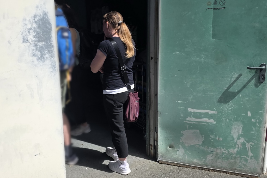 Eine Frau mit Zopf steht draußen vor der offenen Tür zu der Lackiererei von Gawron & Co und blickt in den dunklen Raum.