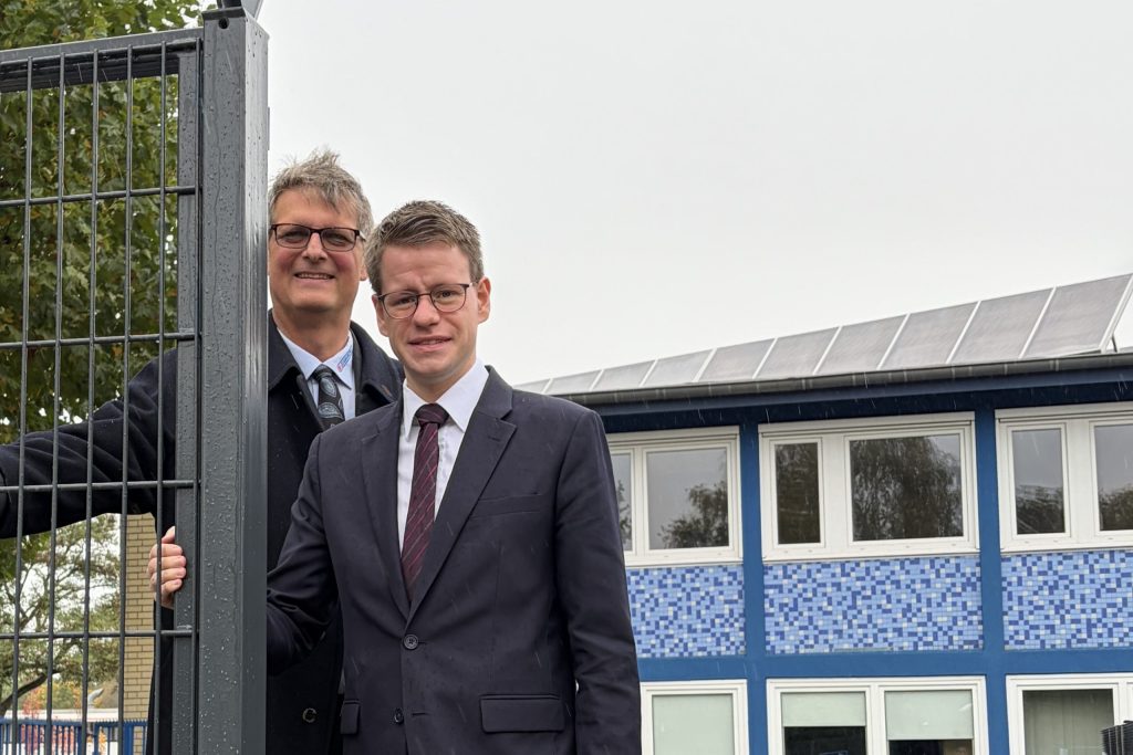 Volker Gawron und der Bundestagsabgeordnete Daniel Kölbl stehen auf dem Hof des Metallbauunternehmens Gawron in Rellingen neben einem Stahlmattenzaun. Rechts im Hintergrund die markante blau geflieste Fassade des Firmengebäudes aus den 60er Jahren.